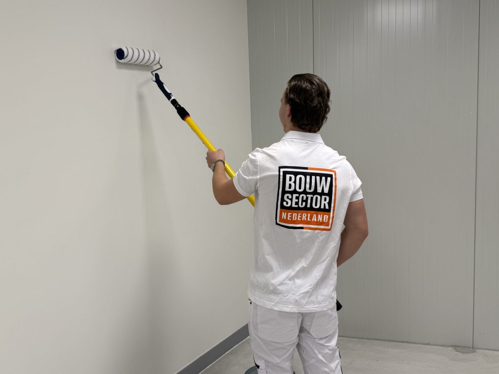 Schilder rolt een witte wand af in een lege ruimte met grijze plint