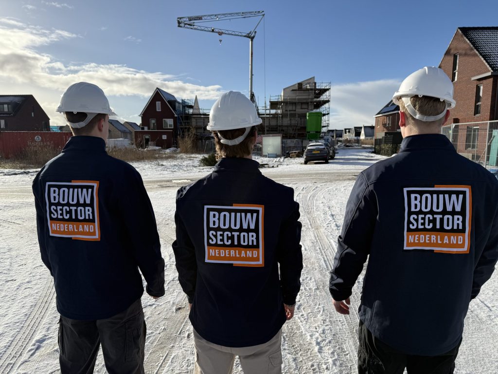 Drie vakmensen in werkjassen met logo kijken naar rijen nieuwe woningen op een winterdag